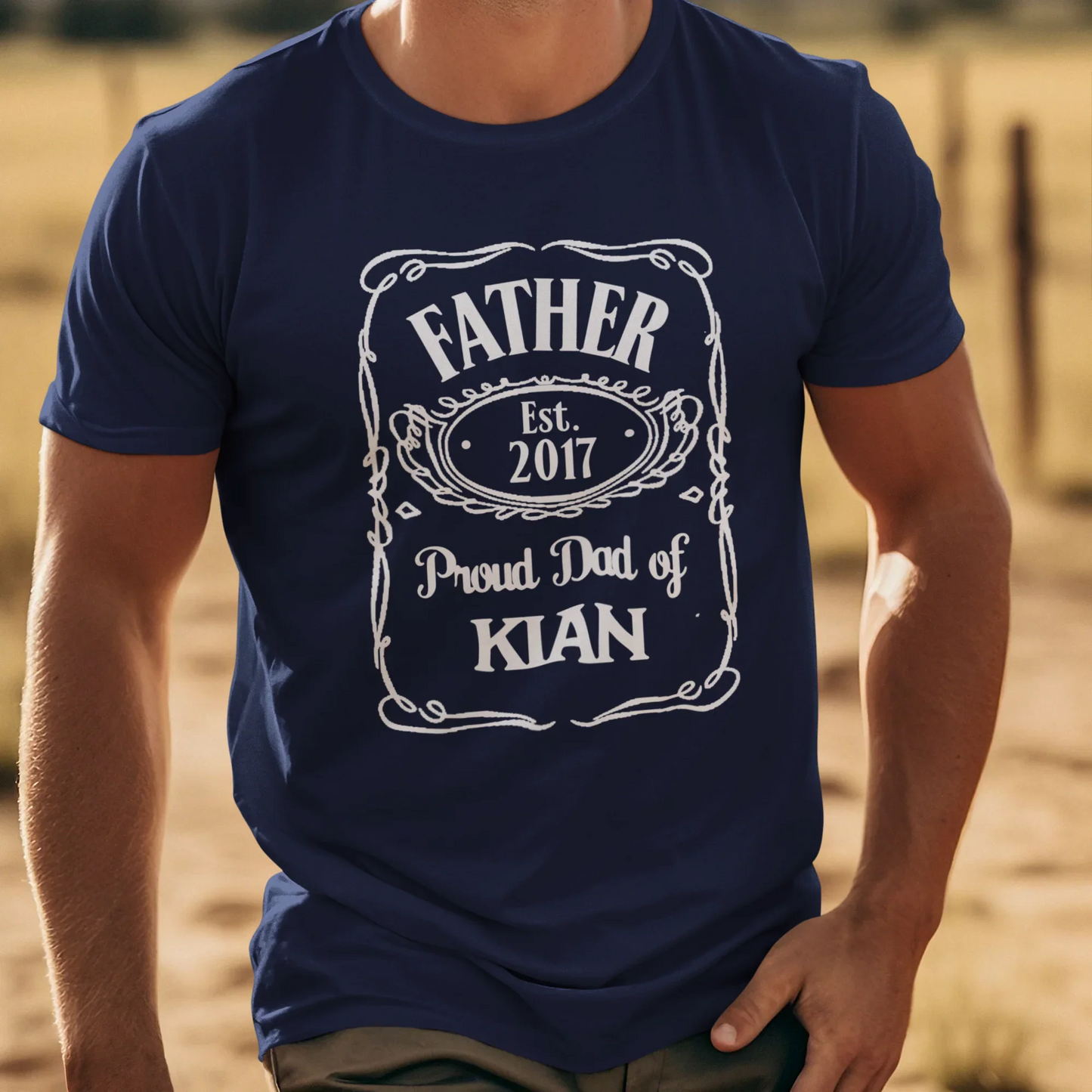 UrbanWarriorStore T-Shirt Mockup: Fröhlicher Mann mit Cowboyhut in Western-Landschaft, "Father Est. 2017 Proud Dad of Kian" Motiv.