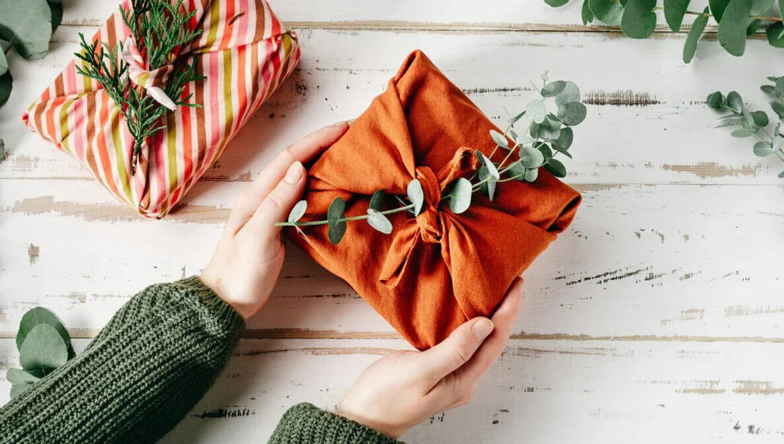 Nachhaltige Geschenke: Geschenk in orangefarbenem Tuch mit Eukalyptuszweig, natürliche Verpackung