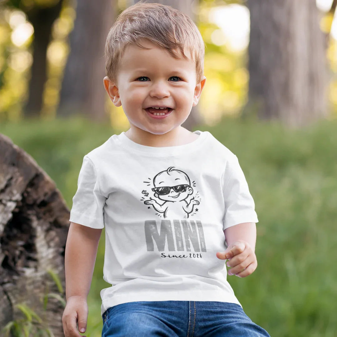 MINI Since 2021 Kinder T-Shirt, lachender Junge im weißen Shirt mit Baby-Motiv im Park