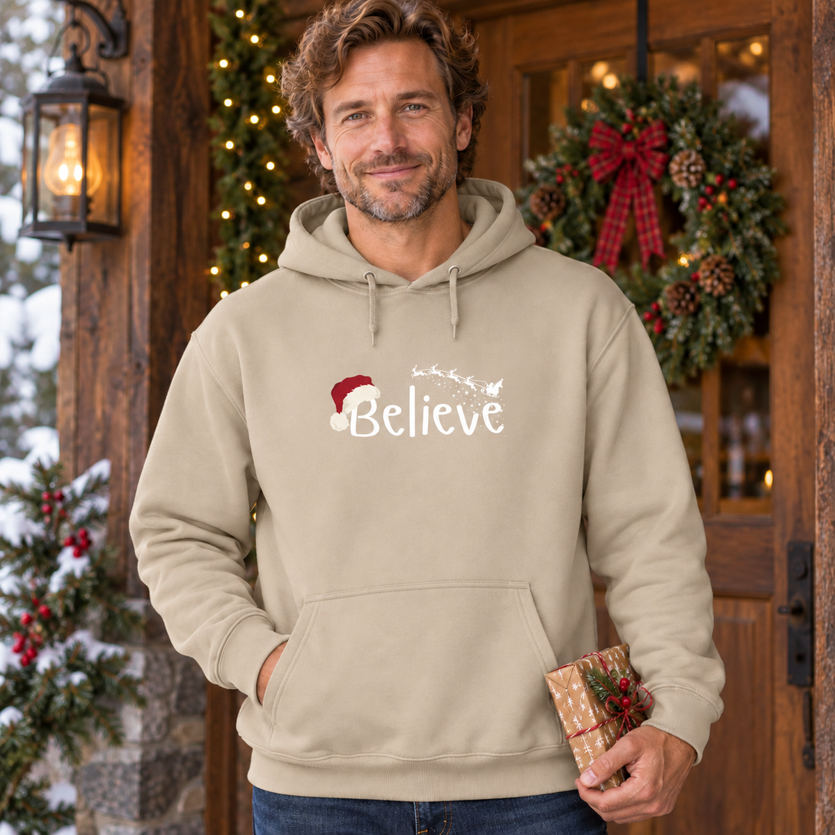 Believe Weihnachts-Hoodie – Sand – weißes Brustmotiv, männliches Model in weihnachtlicher Umgebung