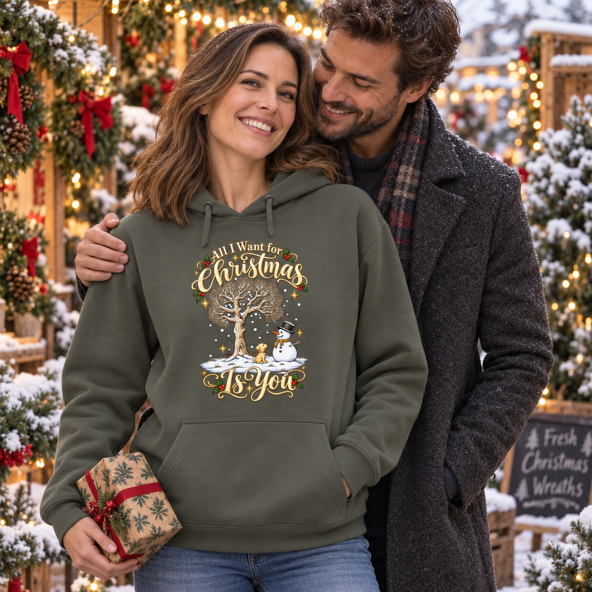 All I Want for Christmas Is You Hoodie in Army – Frau mit Partner und Geschenk am weihnachtlichen Kranzstand